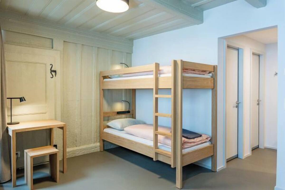 A bunk bed room with a desk and lamp, wooden walls, and a door.