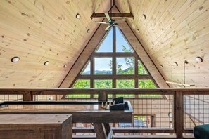 A wooden interior with a sloped ceiling, large windows, and a ceiling fan.