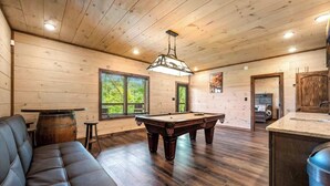 A wooden-paneled room with a pool table, a sofa, and a bar area.
