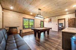 A wooden-paneled room with a pool table, a sofa, and a bar area.