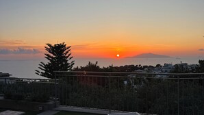 A rooftop terrace with two sun loungers, a view of the sunset over the sea, and a distant cityscape. - La Minucciola (Anacapri)