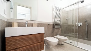 A modern bathroom with a wooden vanity, a toilet, a bidet, and a glass-enclosed shower area. - La Minucciola (Anacapri)