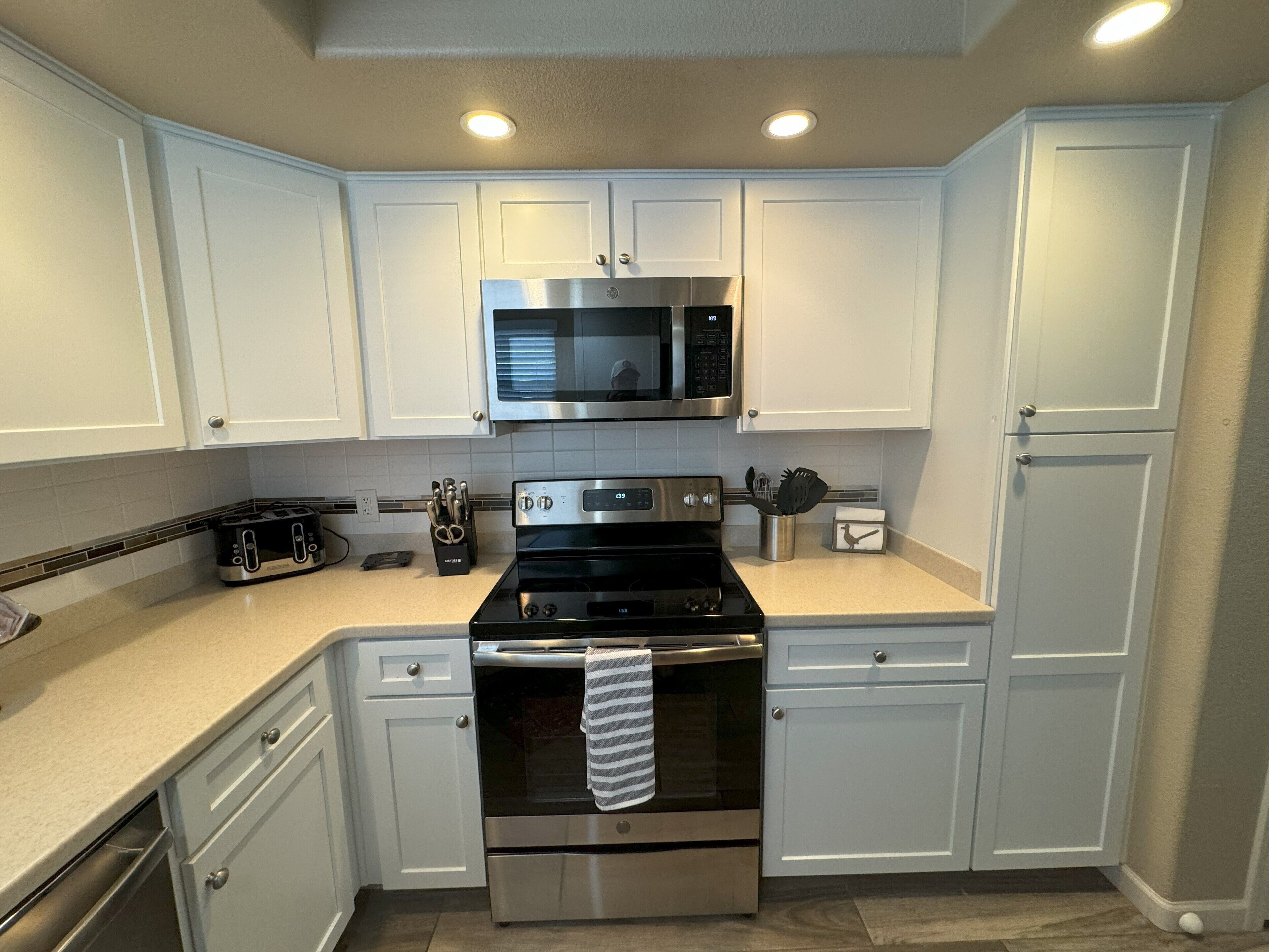 A modern kitchen with white cabinets, stainless steel appliances, and a microwave above the stove.