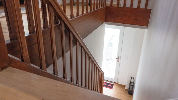 A wooden staircase leading to a second floor with a view of a door and a red mat at the bottom.