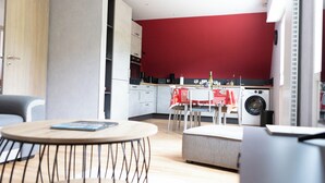A modern kitchen with red walls, a dining area with a table and chairs, and a washing machine.