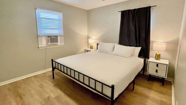Een slaapkamer met een bed, twee nachtkastjes met lampen, een plafondventilator, een raam met jaloezieën en een zwart gordijn.