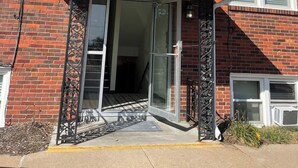Een tweelaags gebouw van baksteen met een overdekte ingang en een schuifdeur van glas.