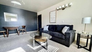 Een moderne woonkamer met een donkerblauwe bank, een glazen salontafel en een klein bijzettafeltje.