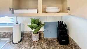 Een keuken met een inbouwkastje met witte servies, glazen en een bloempot.