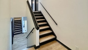 Un escalier moderne avec des marches en bois et des rampes noires, menant à un palier doté d’une porte en verre.