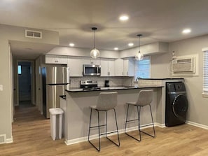 A modern kitchen with stainless steel appliances, a central island with bar stools, and a built-in washer and dryer. - Modern Apartment Near UNMC & Walkable Dining (Omaha)