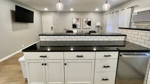 A modern kitchen with white cabinets, black countertops, and a built-in dishwasher.
