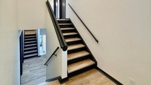 A modern staircase with wooden steps and black handrails, leading to a landing with a glass door.