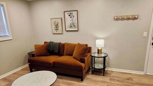 A living room with a brown sofa, a round coffee table, and two side tables with lamps. There are two framed pictures on the wall.