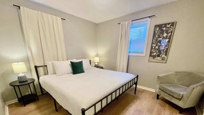 A neatly arranged bedroom with a bed, bedside tables, a chair, and a window with curtains.