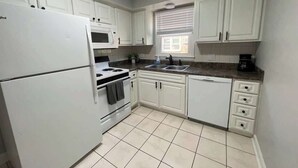 A compact kitchen with white cabinets, a refrigerator, a stove, a microwave, and a sink.