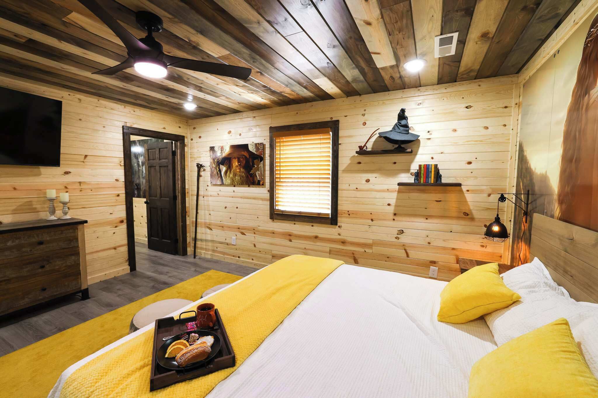 Um quarto tipo cabana de madeira com cama, mesa de cabeceira e televisão montada na parede.