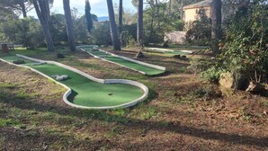 A miniature golf course with green artificial turf and white borders, surrounded by trees and a building in the background. - PLEASANT LITTLE STUDIO IN SAINT-RAPHAËL  (Saint-Raphaël)