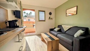 A compact living space with a kitchenette, a sofa, a coffee table, and a balcony with a view of palm trees. - PLEASANT LITTLE STUDIO IN SAINT-RAPHAËL  (Saint-Raphaël)