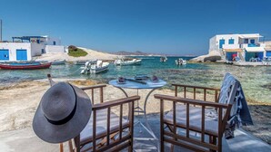A seaside view with a table and chairs, boats, and white buildings with blue accents. - FANI DREAM SUITE By Vilos Suites (Milos)