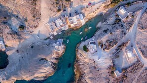 An aerial view of a coastal area with a series of buildings along a narrow waterway, surrounded by rocky terrain. - FANI DREAM SUITE By Vilos Suites (Milos)