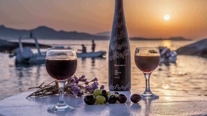 Two glasses of red wine, a bottle, and grapes on a table by the water at sunset. - FANI DREAM SUITE By Vilos Suites (Milos)