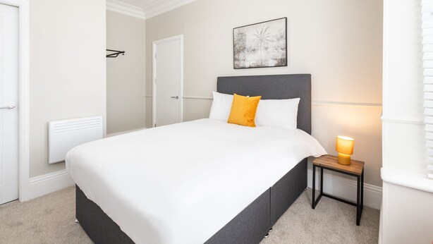 A neatly arranged bedroom with a bed, a bedside table with a lamp, and a door. - Host & Stay | Clifton Studio 1 (Darlington)