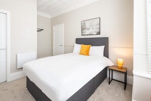 A neatly arranged bedroom with a bed, a bedside table with a lamp, and a door.