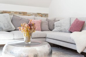 A living room with a grey sofa, a round coffee table, and a vase with dried flowers.