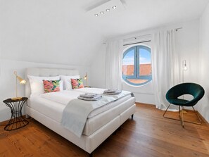 A bedroom with a bed, a chair, a window, and a lamp.