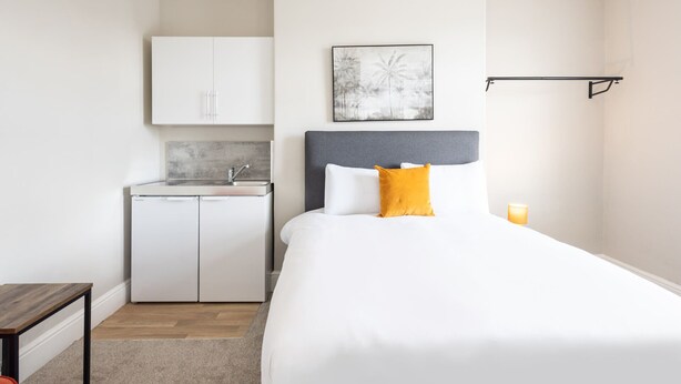 A bedroom with a bed, a bedside table, a nightstand, a small kitchenette, and a wall-mounted shelf. - Host & Stay | Clifton Studio 4 (Darlington)