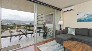 A living room with a sofa, coffee table, and a view of a balcony with a dining area.