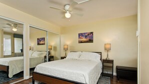 A bedroom with a bed, a ceiling fan, a large mirror, and a painting on the wall.