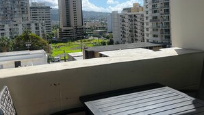 A balcony with a table and chairs, overlooking a cityscape with tall buildings and a green park. - Mellow Kuhio Village Studio | Private Lanai (Honolulu)