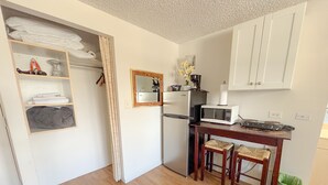A compact kitchen with a refrigerator, microwave, and wooden table with two chairs. - Mellow Kuhio Village Studio | Private Lanai (Honolulu)