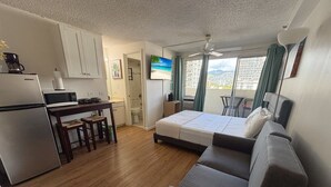 A compact living space with a kitchenette, a sofa, a dining table, and a view of the city. - Mellow Kuhio Village Studio | Private Lanai (Honolulu)