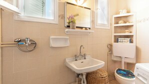 Une salle de bain équipée d’un lavabo, d’un miroir, de toilettes et d’étagères où sont rangés les produits de toilette.
