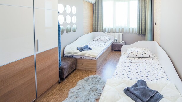 Ein modernes Schlafzimmer mit zwei Betten, einem Kleiderschrank, einer Spiegelwand und einem Fenster mit Vorhängen.