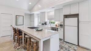 A modern kitchen with white cabinetry, a marble island, and a patterned rug.