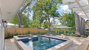 A backyard with a swimming pool, wooden deck, and a covered patio area.