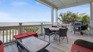 Ett takförsett utomhusområde med ett bord och stolar, en grill och utsikt över havet.