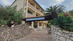 A hotel entrance with a stone wall, a sign reading "Hotel Fontolleccio," and a paved path leading to the building. - Hotel Fontalleccio (Marciana)