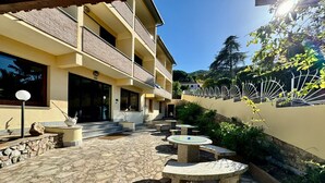 A courtyard with stone flooring, outdoor seating, and a building with multiple balconies. - Hotel Fontalleccio (Marciana)