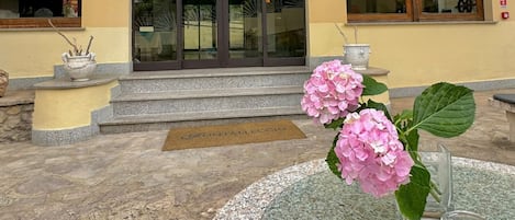 A hotel entrance with a yellow facade, a glass door, and a small outdoor seating area with a table and flowers.