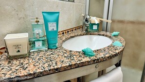 A bathroom with a granite countertop, a white sink, and various toiletries including a bottle of ACQUA DELL'ELBA CLASSICA gel, a blue tube of ACQUA DELL'ELBA CLASSICA shampoo, and a white ACQUA DELL'ELBA candle. - Hotel Fontalleccio (Marciana)