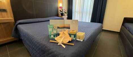 A hotel room with a large bed, a nightstand, a wall-mounted lamp, and a window with curtains.