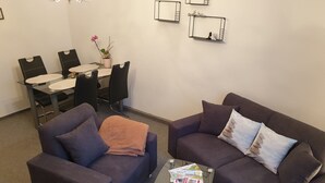 A living room with two sofas, a coffee table, a dining table with chairs, and wall-mounted shelves. - Gästehaus mit Fewos, Apartments und Zimmern im Thüringer Wald - Familientreffen! (Siegmundsburg)