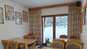 A dining area with a wooden table and chairs, a potted plant, and a view of a snowy landscape through a glass door. - Gästehaus mit Fewos, Apartments und Zimmern im Thüringer Wald - Familientreffen! (Siegmundsburg)