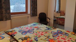 A bedroom with a bed covered in a floral and butterfly quilt, a window with a view of a snowy landscape, a chair, and a wardrobe. - Gästehaus mit Fewos, Apartments und Zimmern im Thüringer Wald - Familientreffen! (Siegmundsburg)
