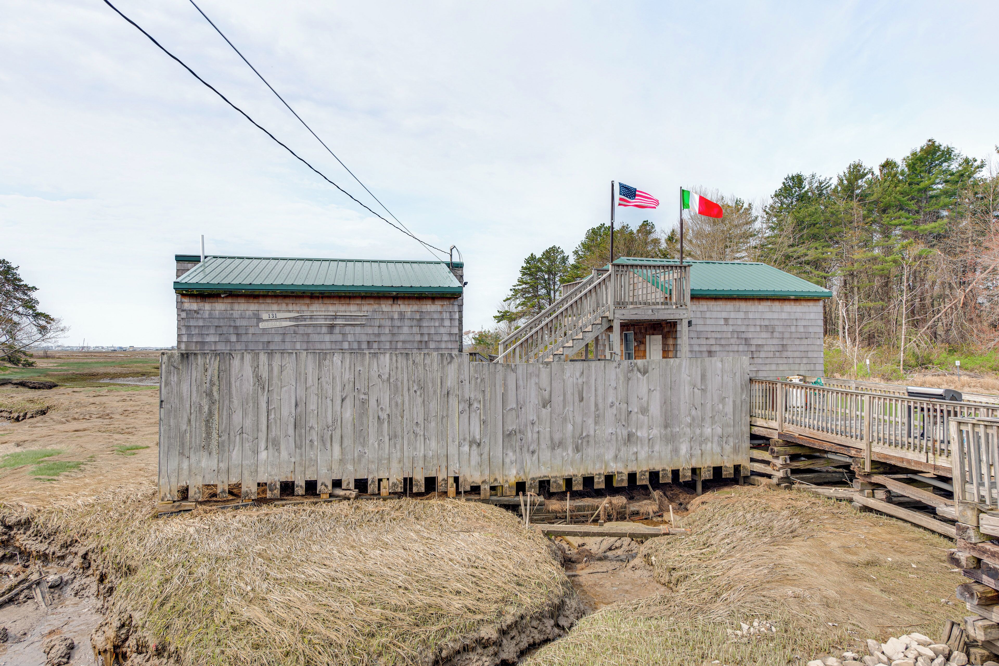 A wooden structure with a green roof, a flagpole with an American flag, and a flagpole with a flag that appears to be the Italian flag.